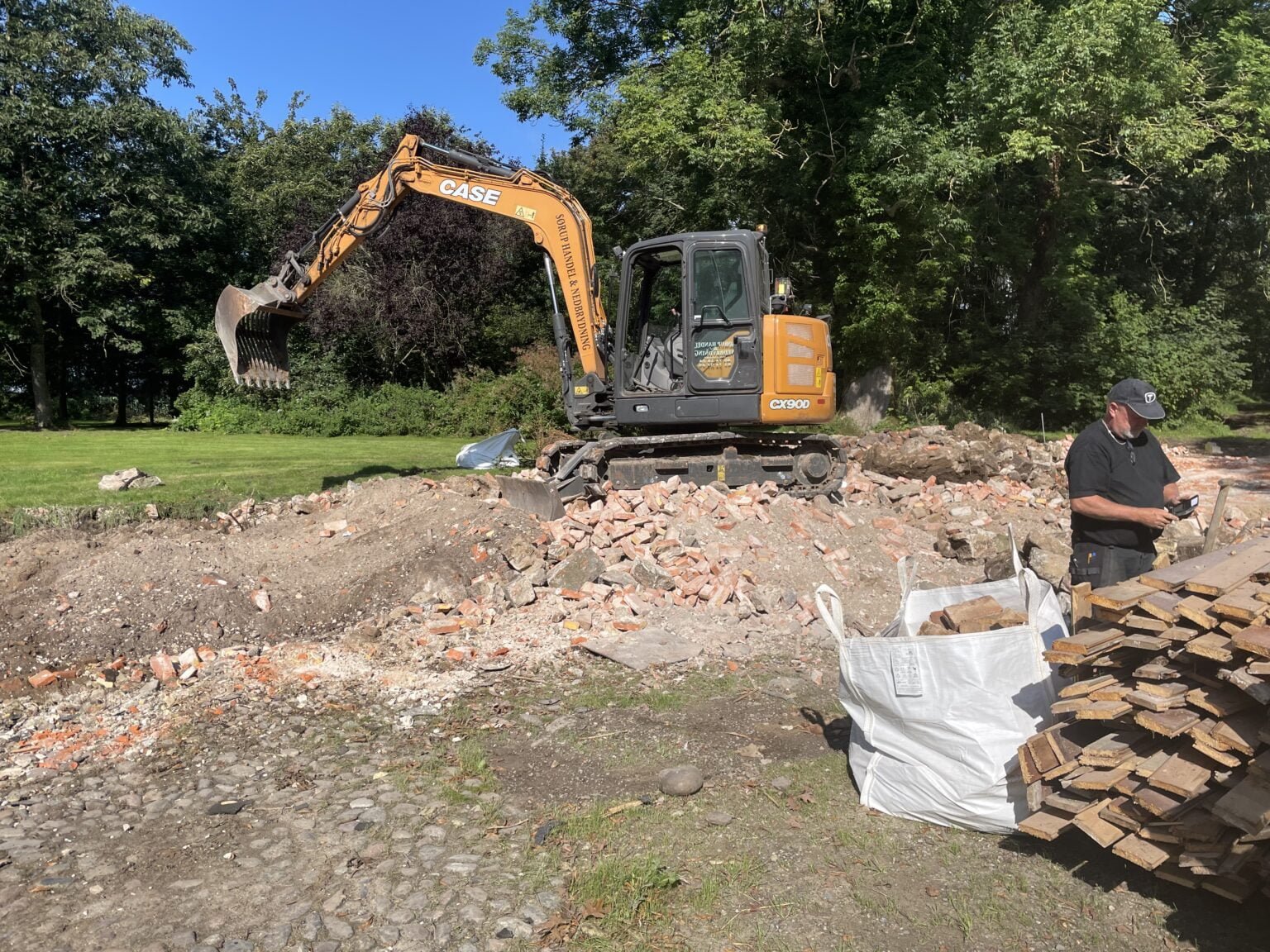 Gravemaskine rydder byggeplads med murbrokker og træ.